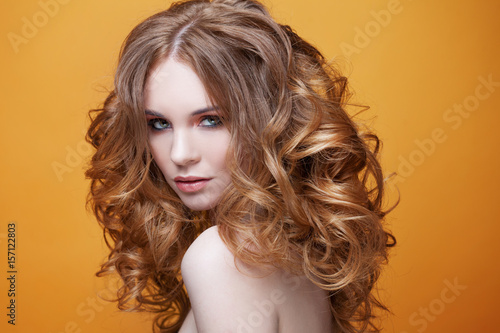 Beautiful redheaded girl with luxurious curly hair. Studio portrait on yellow background. Excellent hair