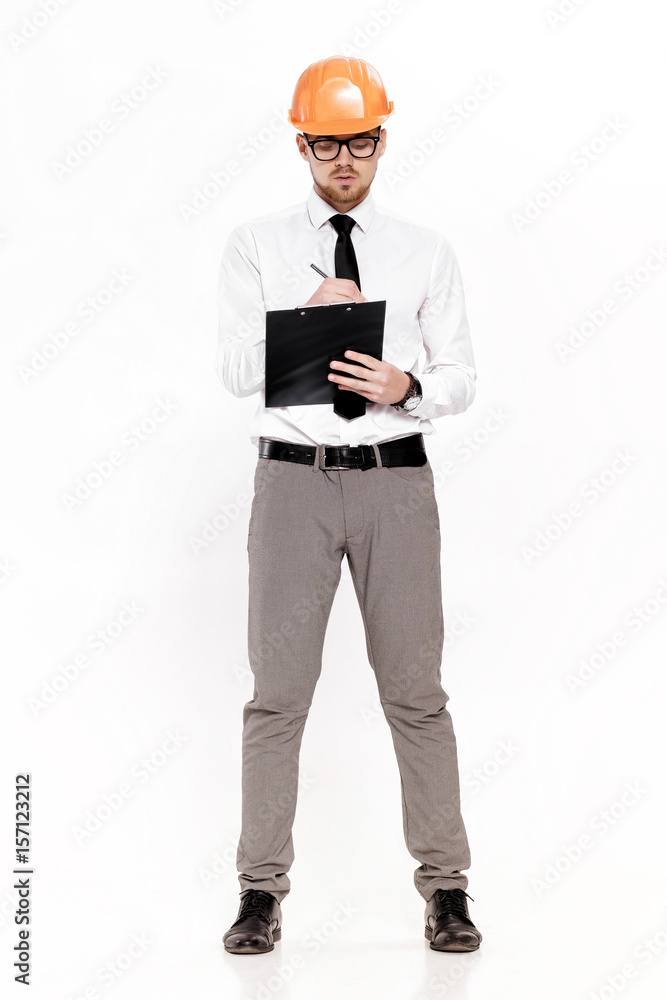 Young construction engineer in orange helmet writes in folder on white background Young construction engineer in orange helmet writes in folder on white background