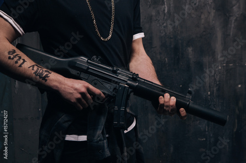 Unrecognizable killer with sniper rifle closeup studio shoot. Armed white gangster man with weapon and tattoo on dark background. Outlaw, ghetto, murderer, robbery concept