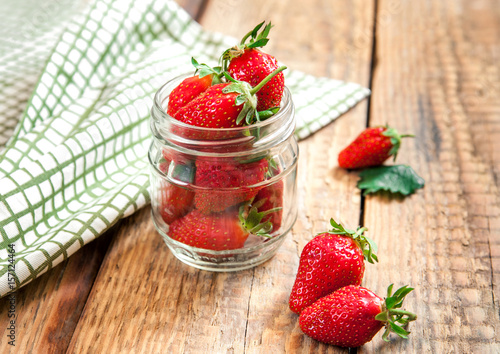 Fresh ripe strawberry in a glass jar on an old wooden table. Organic healthy fruit dessert.