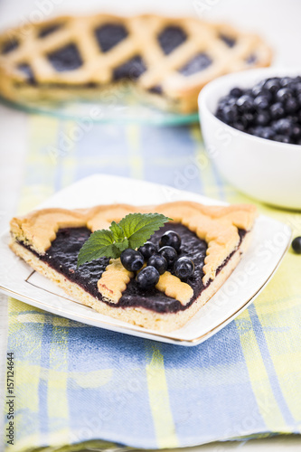 Piece of a blueberry pie and fresh berries on a wooden table.
