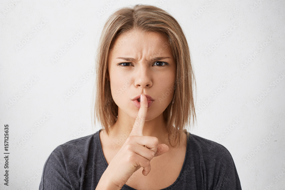 Be silent! Beautiful young Caucasian woman with stylish hairdo dressed casually holding finger at her lips asking to be quiet having angry expression. Secrecy and concealing important information Be silent! Beautiful young Caucasian woman with stylish hairdo dressed casually holding finger at her lips asking to be quiet having angry expression. Secrecy and concealing important information