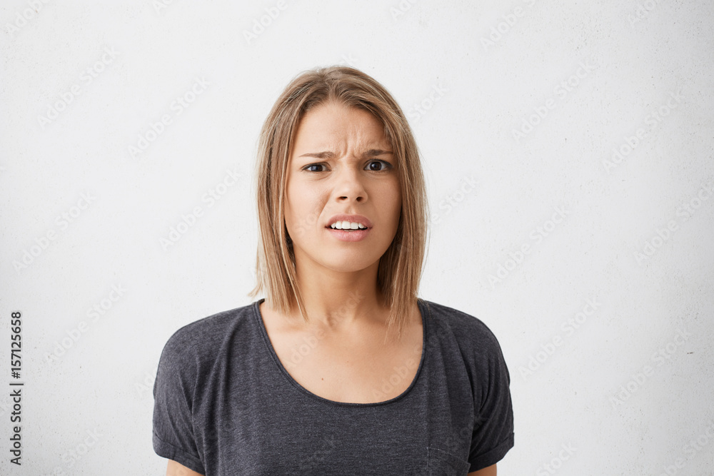 Medium close-up of dissatisfied pretty woman with coloured straight hair and dark eyes wearing casual clothes having displeased look and opened mouth while posing in studio against white background Medium close-up of dissatisfied pretty woman with coloured straight hair and dark eyes wearing casual clothes having displeased look and opened mouth while posing in studio against white background