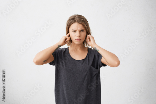 Wallpaper Mural Unhappy stressed out teenage girl with tattoos on arms plugging ears with fingers doesn't want to hear annoying noise or ignoring stressful and unpleasant situation or conflict. Body language Torontodigital.ca
