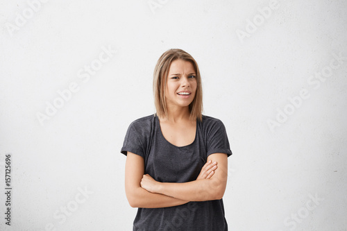 Studio shot of attracive doubtful and dissatisfied young woman having skeptical and suspicious look, keeping arms folded, expressing suspicion or doubt. Human emotions, reaction and attitude