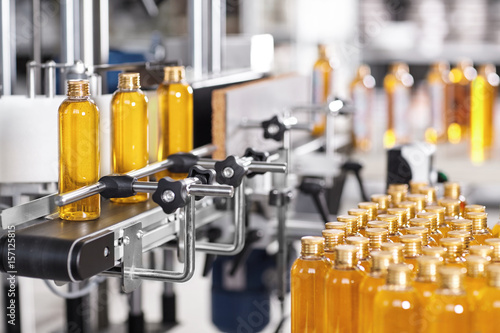 Production line of beauty and healthcare products at plant or factory. Process of manufacturing and packaging cosmetics goods. Glass or plastic bottles with screw caps standing on conveyor belt photo