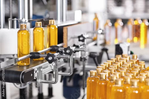 Obraz Production line of beauty and healthcare products at plant or factory. Process of manufacturing and packaging cosmetics goods. Glass or plastic bottles with screw caps standing on conveyor belt