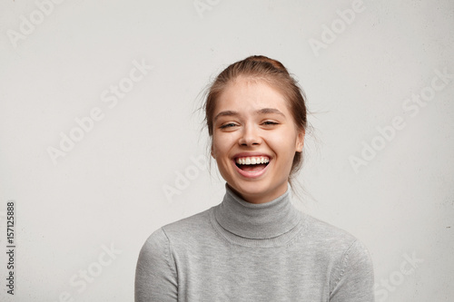 Headshot of good-looking lucky woman with tied hair pure skin and broad smile being happy to watch at camera. Sincere female with beautiful appearance wearing casual clothes isolated over white wall