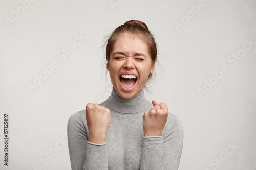 Foto Cheering happy young Caucasian female with pure skin and beautiful appearance clenching fists being excited of success