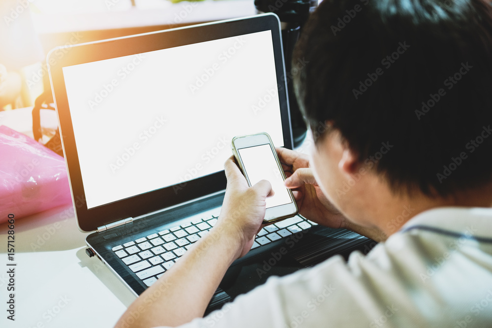 a guy working using computer laptop, and smart phone with blank white screen a guy working using computer laptop, and smart phone with blank white screen