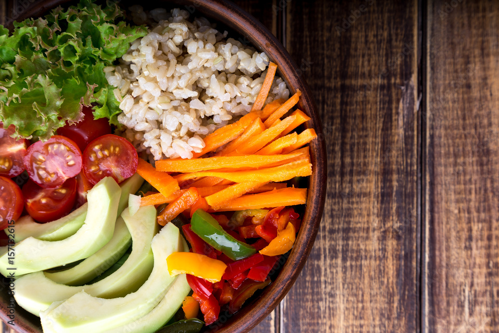 Vegan buddha bowl on wooden background. Top view. Bowl with carrot, lettuce, tomatoes cherry, pepper, avocado and porridge. Vegetarian, healthy, detox food concept.