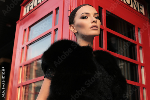 beautiful girl with dark hair walking by the street, red phone booth on background