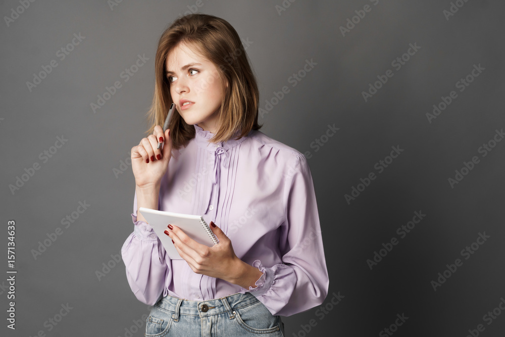 Fototapeta premium Business woman holds a notebook with a pen. Something writes and thinks. Studio photography. One on a gray background.