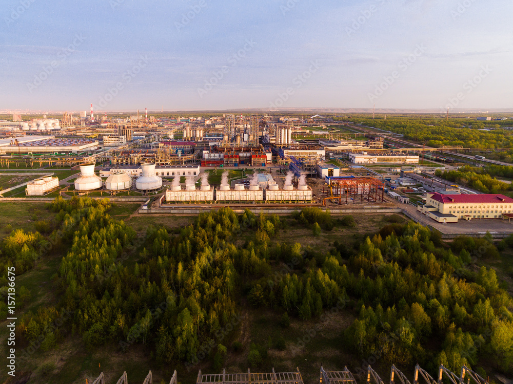 A huge oil refinery with pipes and distillation of the complex on a green field surrounded by forest. Aerial view A huge oil refinery with pipes and distillation of the complex on a green field surrounded by forest. Aerial view