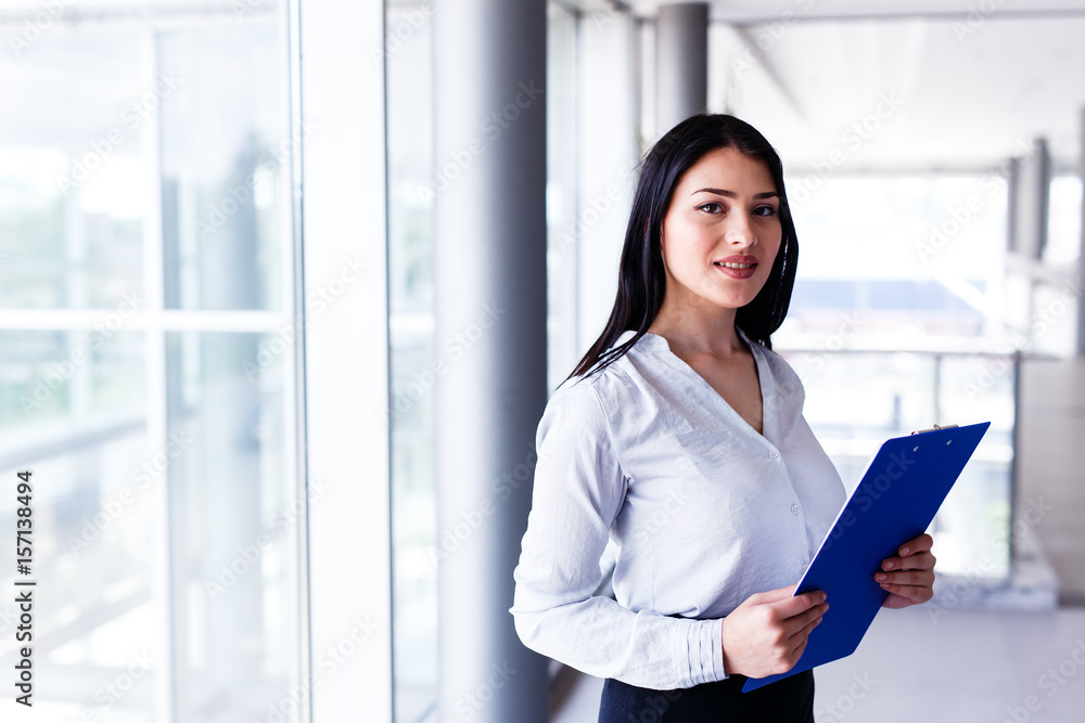 Attractive woman standing in business building with paper board in her hands Attractive woman standing in business building with paper board in her hands