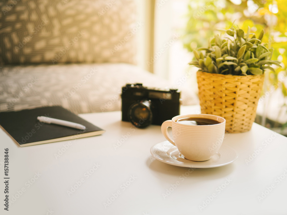 coffee cup, Retro camera, notebook, white pen and Plastic plants on white table in the coffeeshop the sun's rays in the morning coffee cup, Retro camera, notebook, white pen and Plastic plants on white table in the coffeeshop the sun's rays in the morning