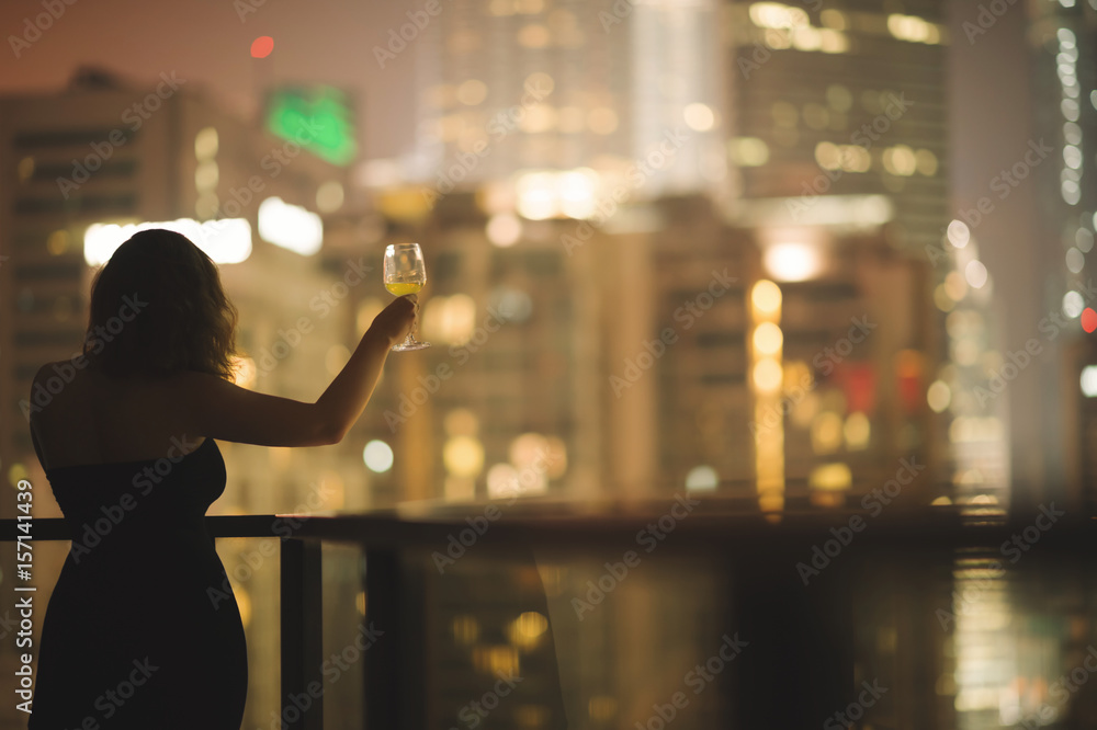 Φωτογραφία Beautiful young woman on the balcony in a black dress with a glass of wine on th