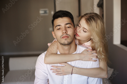 Young romantic couple at home. Caucasian blonde woman and brunette man. Lovers hugging in living room.