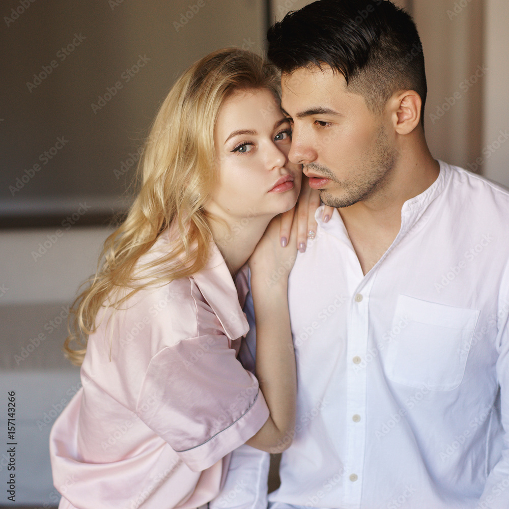 Young romantic couple at home. Caucasian blonde woman and brunette man. Lovers hugging in living room.