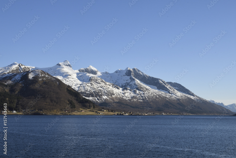 Clear blue water and the village Bratland and snowy mountains in background