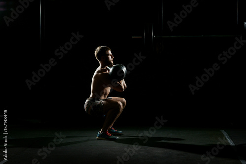 Fitness training. Man doing sit ups with weights in dark gym.
