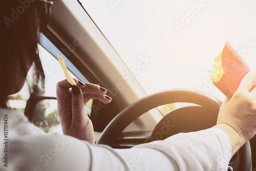 Lady eating french fries white driving car dangerously