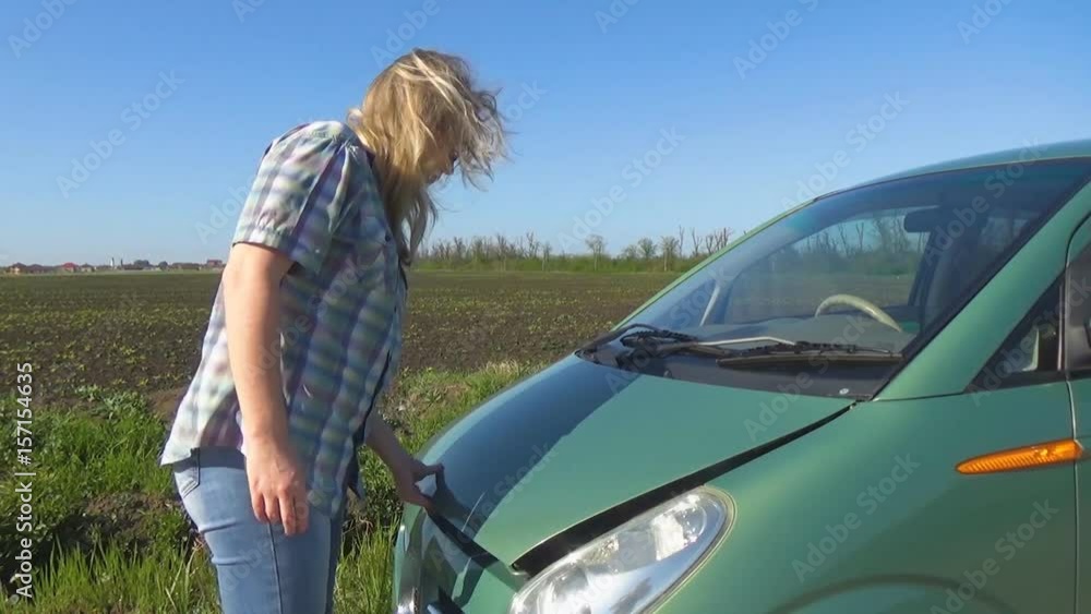 The girl with glasses and plaid shirt bypasses the car and opens the hood. A woman in a broken car. The girl with glasses and plaid shirt bypasses the car and opens the hood. A woman in a broken car.