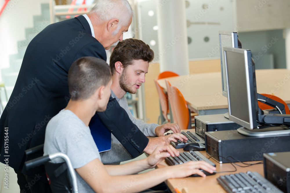 Teacher helping young men using computers, one in wheelchair Stock ...