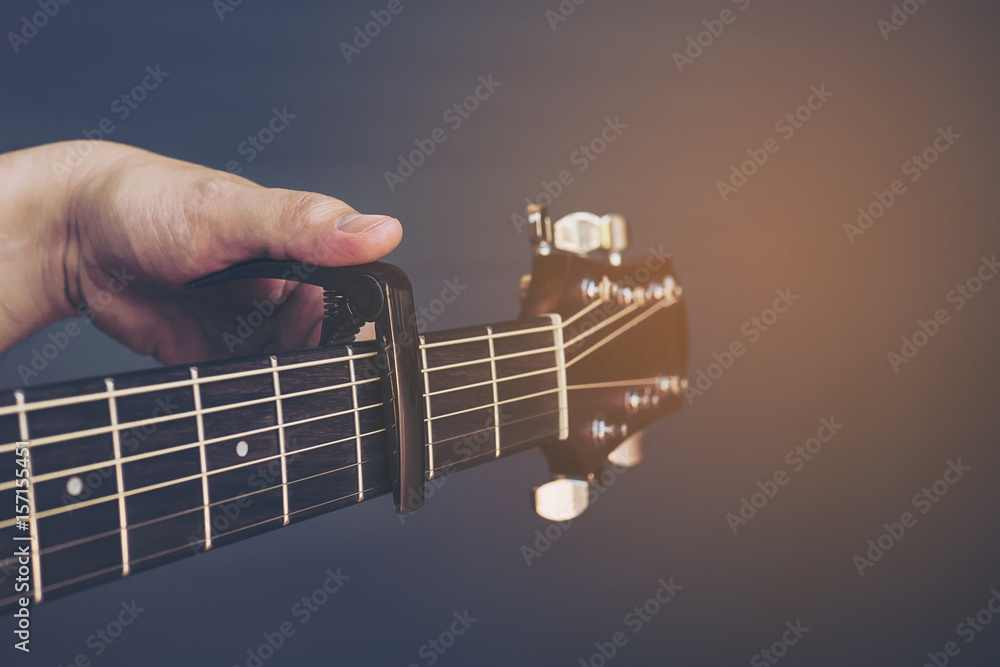 Fototapeta premium Vintage color picture of man putting guitar capo over gray background