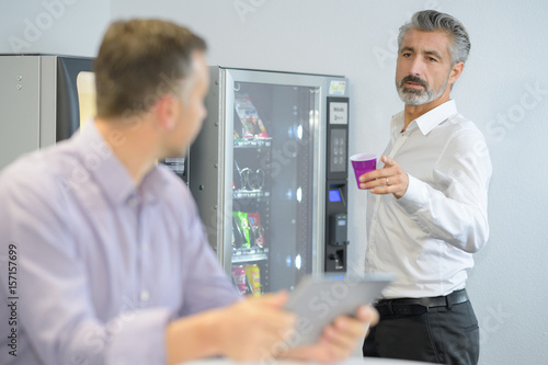 Quadro su tela Businessman offering coffee from vending machine
