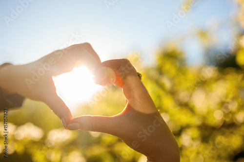 Female hands heart shape on nature green bokeh sun light flare and blur leaf abstract background. Copy space of happy love and freedom concept.