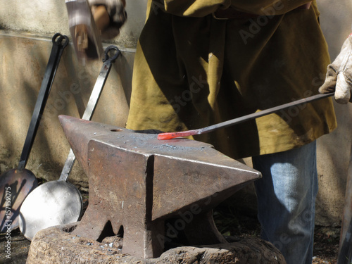 Blacksmith manually forging the molten metal with hammer on the anvil