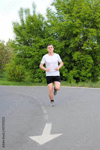 молодой спортсмен бежит по беговой асфальтированной дорожке в парке летом