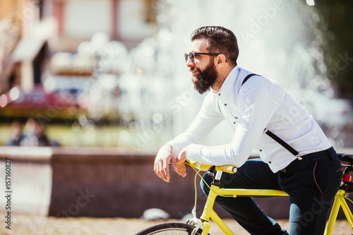 Portrait of handsome young bearded man leaning at his bicycle while standing on fountains outdoors