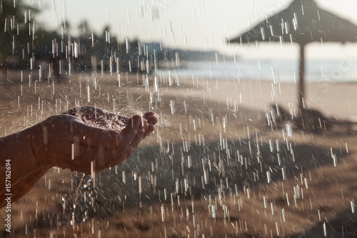 Руки человека и капли душа на фоне морского пляжа.