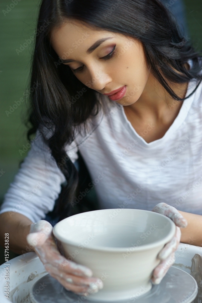 Young beautiful pretty woman with brunette dark hair working on pottery wheel and sculpting clay pot Young beautiful pretty woman with brunette dark hair working on pottery wheel and sculpting clay pot