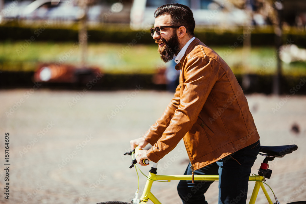 Obraz premium Young bearded man riding on his bicycle outdoors on sunny street
