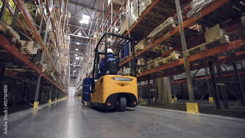 Back view of warehouse worker transporting cargo on forklift