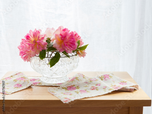 Roses in a cut glass rose bowl on a table with a rose ribbon by the window photo