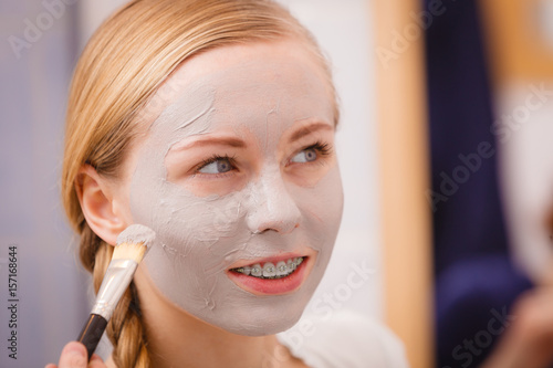Woman applying with brush clay mud mask to her face