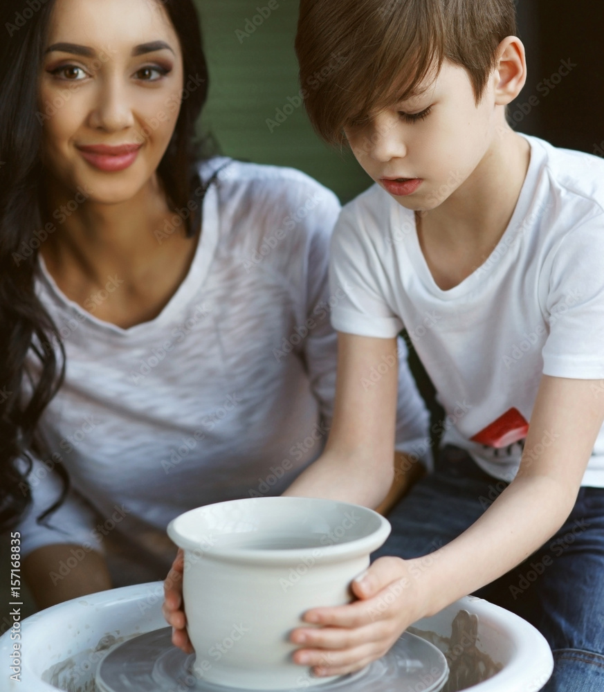 Pottery classes. Young beautiful pretty caucasian brunette mother teaching her son. Son making clay pot on potter wheel Pottery classes. Young beautiful pretty caucasian brunette mother teaching her son. Son making clay pot on potter wheel