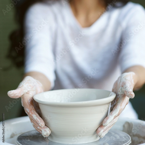 Young beautiful pretty woman with brunette dark hair working on pottery wheel and sculpting clay pot. Shallow DOF. Focus on hands