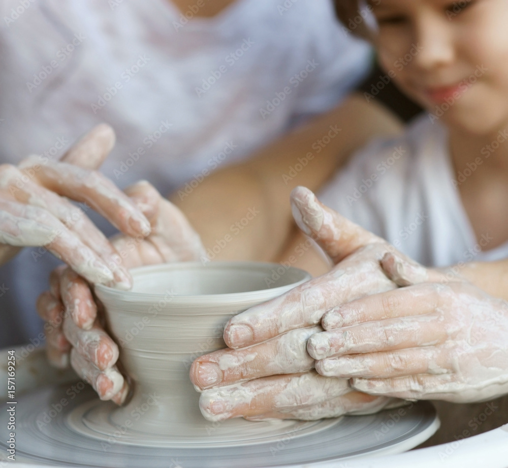 Parents teach their child to work on potter wheel. Father showing how to sculpt clay pot. Closeup of dirty hands. Shallow DOF.