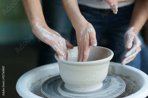 Mother teaches son to work on pottery wheel. Close up of dirty hands sculpting clay.