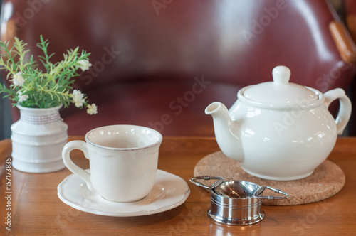 White tea pot and cup with Tea strainer on wooden table, relaxing with hot tea during tea break.