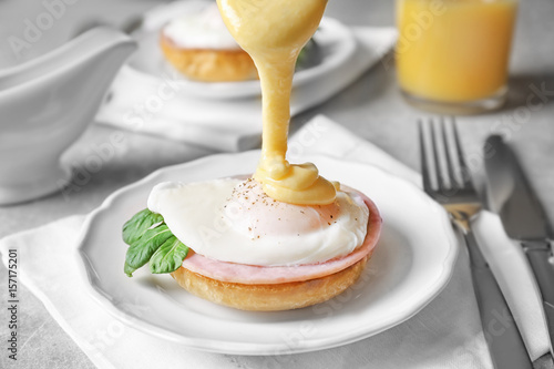 Pouring sauce onto egg Benedict on plate, closeup