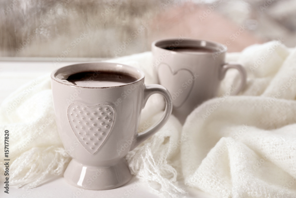 Cups of hot drink with shawl on windowsill