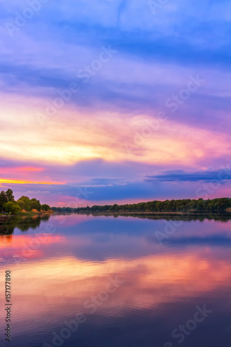 Vivid scenery of sunset at the river, colorful, dramatic evening sky reflected in the water, hdr image. Khmelnytskyi, Ukraine