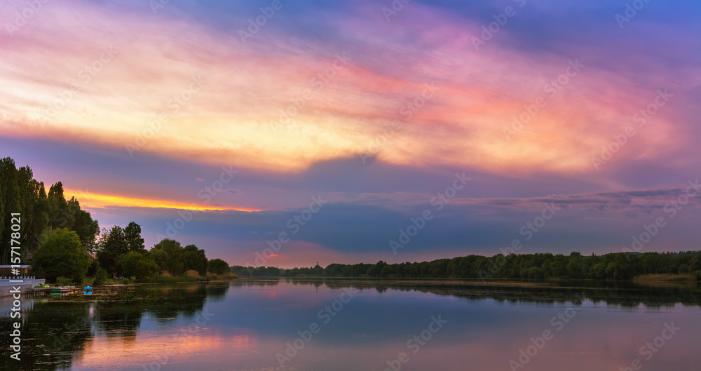 Vivid scenery of sunset at the river, colorful, dramatic evening sky reflected in the water. Khmelnytskyi, Ukraine Vivid scenery of sunset at the river, colorful, dramatic evening sky reflected in the water. Khmelnytskyi, Ukraine