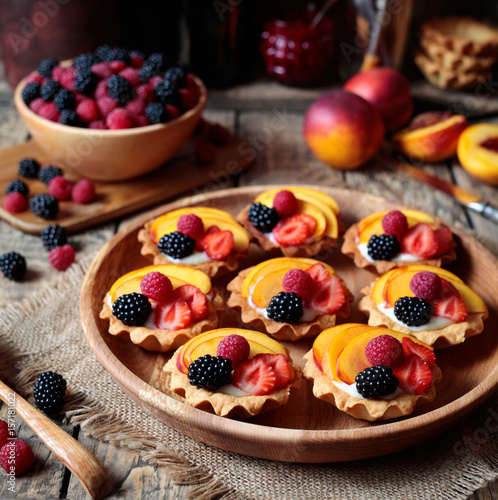 Close up. Summer delicious dessert with various fruits. Fresh berry tartlet or cake with vanilla custard, raspberry, peach and blackberry for the whole family. Rustic style.